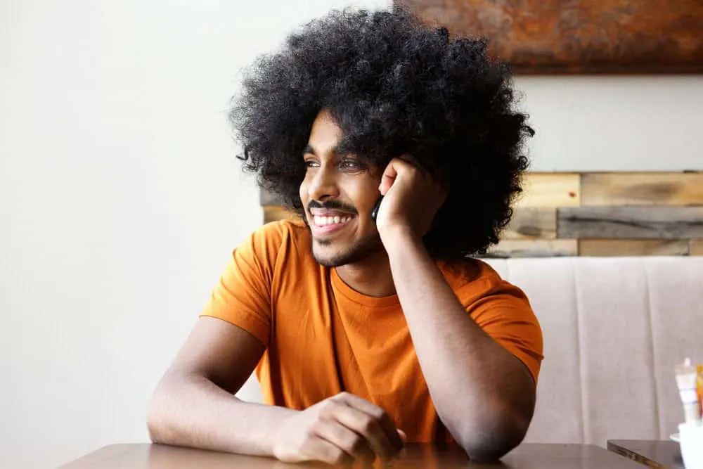 How to Make Your Hair Grow Faster and Thicker as a Black Man 6 A cheerful African American man with long hair styled with castor oil and tea tree oil that's sitting in a coffee shop.