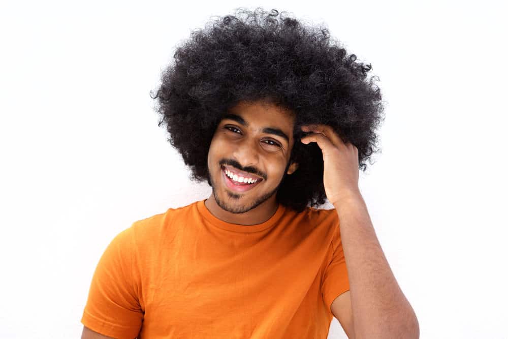 A light-skinned black man with kinky hair uses essential oils to moisturize his coily hair and to promote hair growth.