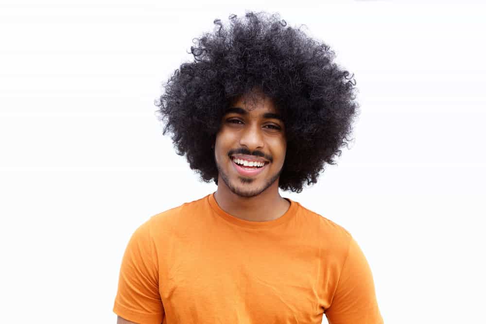 A cheerful man of color with type 4 African hair styled with jojoba oil and scalp massages to promote growth.