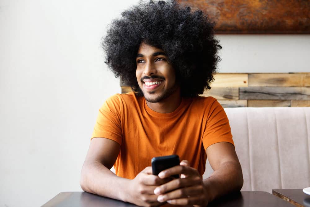 African American male with curly hair strands sitting in a coffee shop waiting for a black coffee and light creamer.