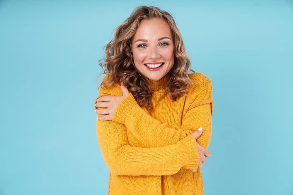 A cheerful young female with dry hair has a type 2 wavy hair texture that's styled with natural oils and curl cream.