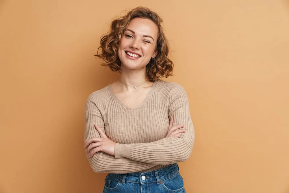12 Best Medium-Length Haircuts With Layers, Bangs, & More 7 A beautiful woman with medium-layered thick hair full of lovely swoopy layers and wispy curtains on a tanned skin tone.