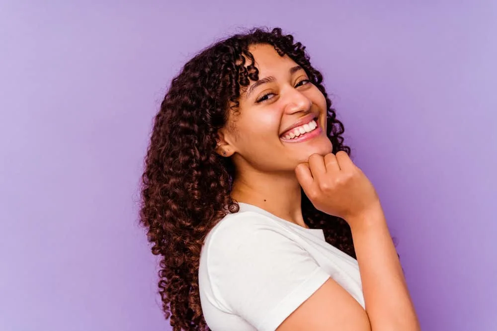 A cute African American female wearing jeans and a white crop top while admiring her appearance.