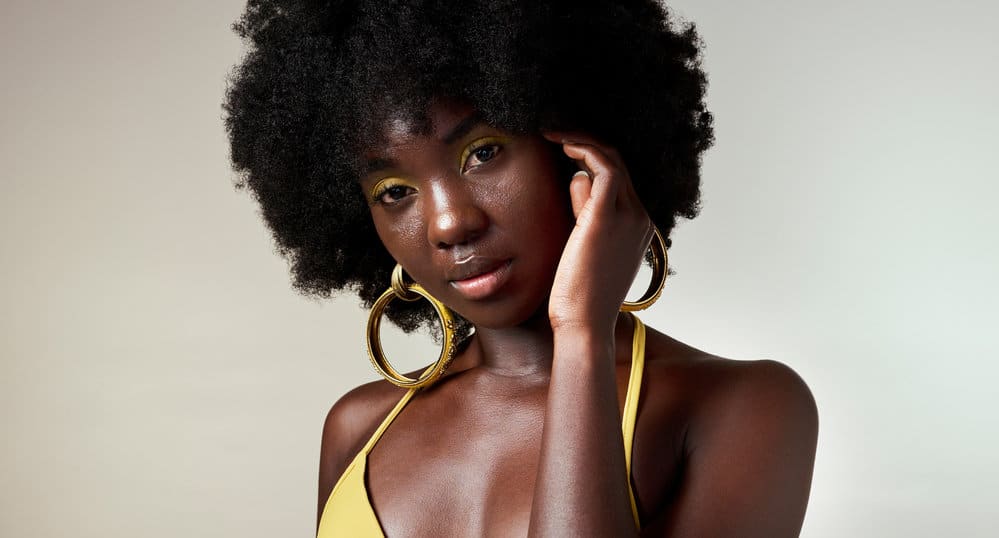 A dark-skinned black girl with dry natural hair used light oils to style and moisturize low-porosity hair stands.