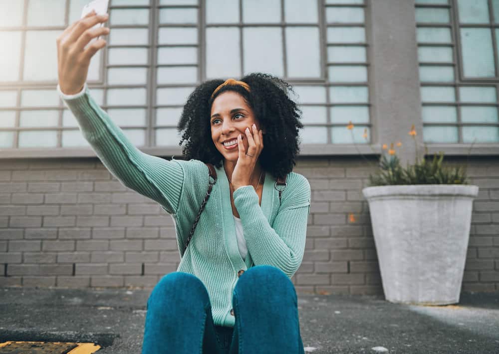 A black girl with clean hair following a conditioner washing hair care routine is taking a selfie photo.