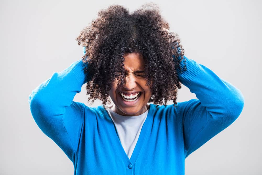 A black girl with shorter hair puts her 4B curl type in an updo with hair clips using the pineapple method.