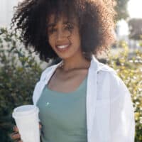 A cute young African American female with naturally curly hair uses the curly girl method to promote hair growth.