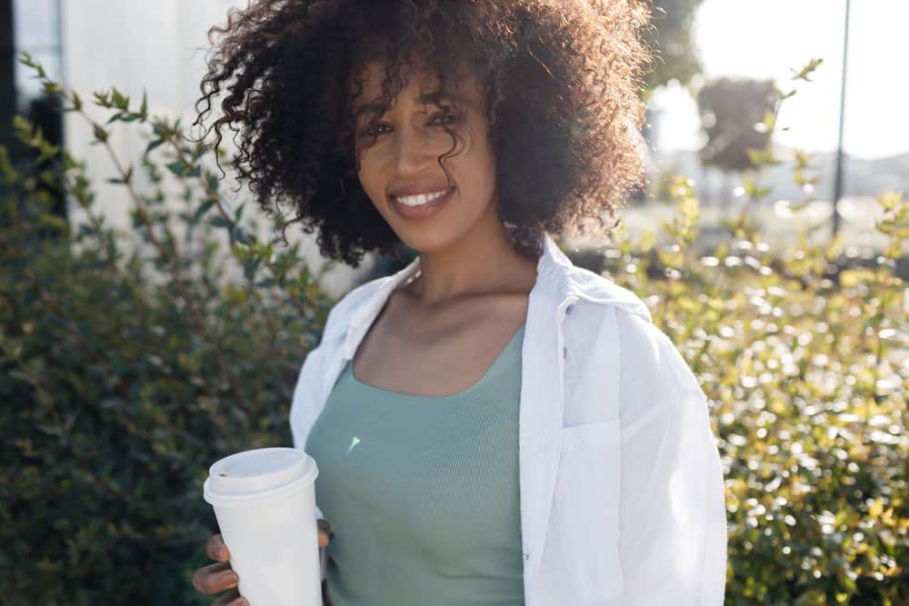 A cute young African American female with naturally curly hair uses the curly girl method to promote hair growth.