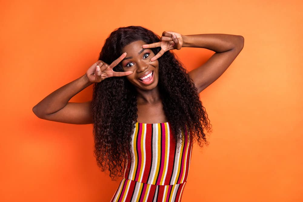 An African American woman that often wears medium-density wigs is wearing a multi-colored outfit.