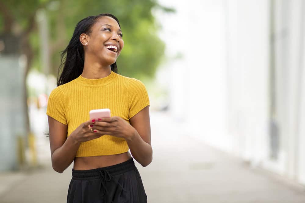 A cheerful black girl with a curly natural texture is reading the blog of a curly hair expert due to hair shaft damage.