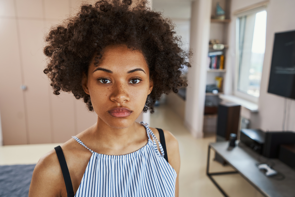 A black girl with a 3C hair type only uses curly girl approved styling products on her dark brown wavy hair stands.