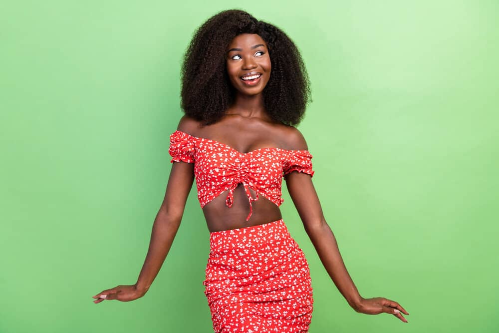 A young lady that often wears hair wigs is wearing a cute curly full lace wig with a casual red top and skirt.
