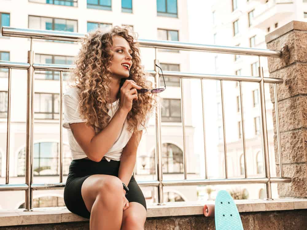 A white girl sitting on a park bench waiting for Sally Beauty Supply store's tint department to open.