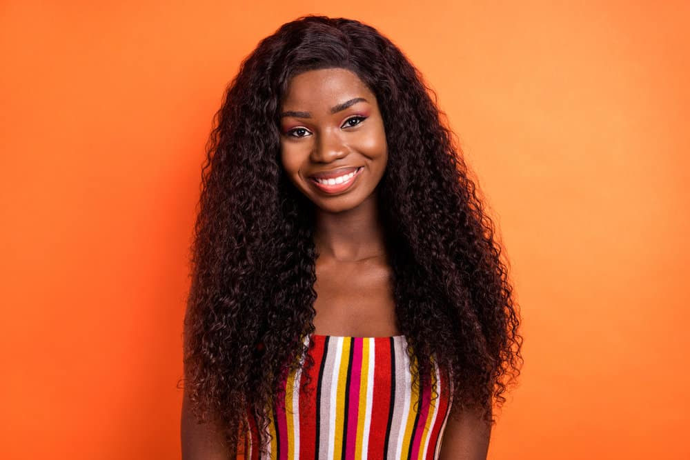 A cute young black girl wearing a curly hair wig with natural-looking long hair follicles with thin hair strands.