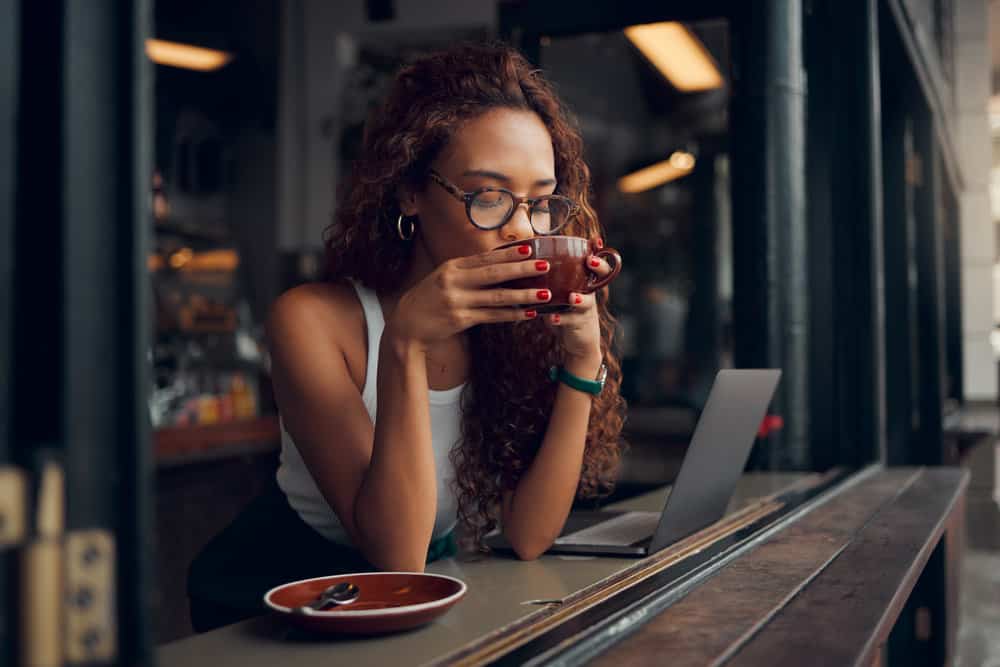 An African American female sitting in a coffee shop researching the scalp's oil production on her laptop.