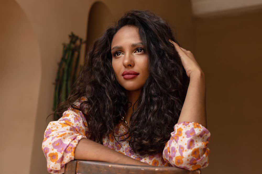 A dark-skinned female with dark brown curls styled with natural hair oils to boost hair growth and mitigate hair fall.