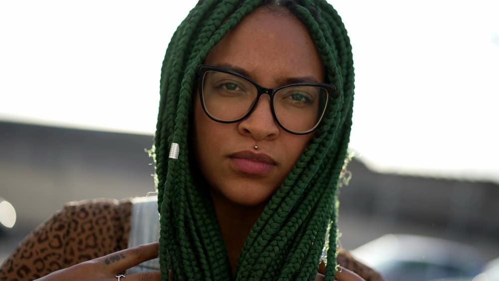 A young lady with black and green box braids moisturized her hair with scalp pomade to mitigate hair loss.