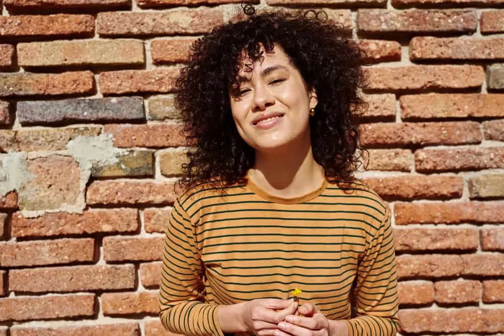 How to Clarify Curly Hair at Home: DIY Clarifying Guide 9 A woman taking a selfie in front of a brick wall after washing hair with a chelating clarifying shampoo.
