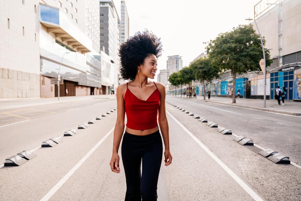 A young female with a casual outfit has curly hair fibers styled with a silicone-free conditioner following the CG method.