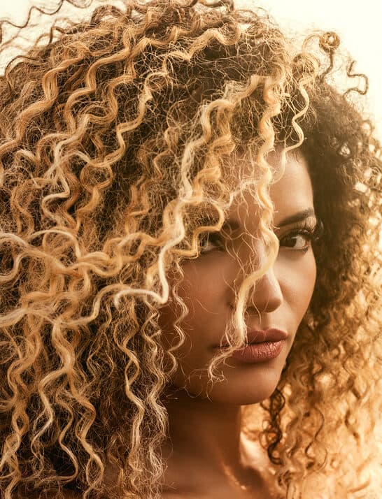 A black girl with towel-dried hair used a pale ash blonde permanent liquid toner on her unwanted orange tones.