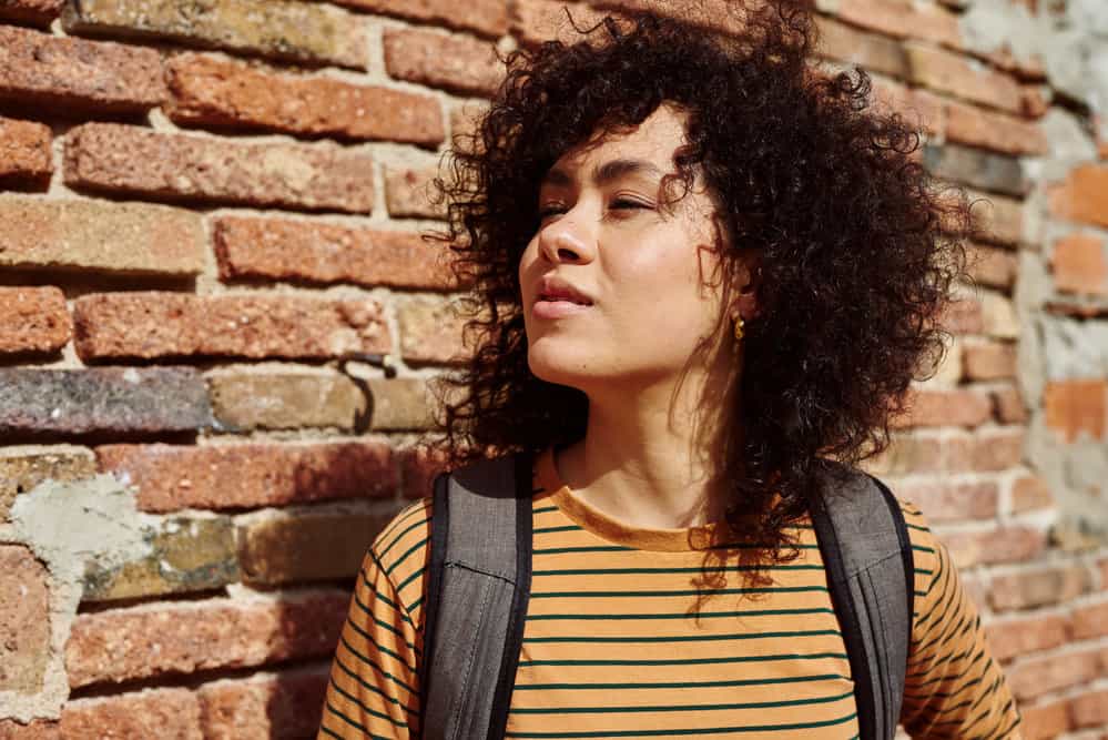 A black girl with color-treated hair follows the curly girl method on her type 3 natural hair strands.