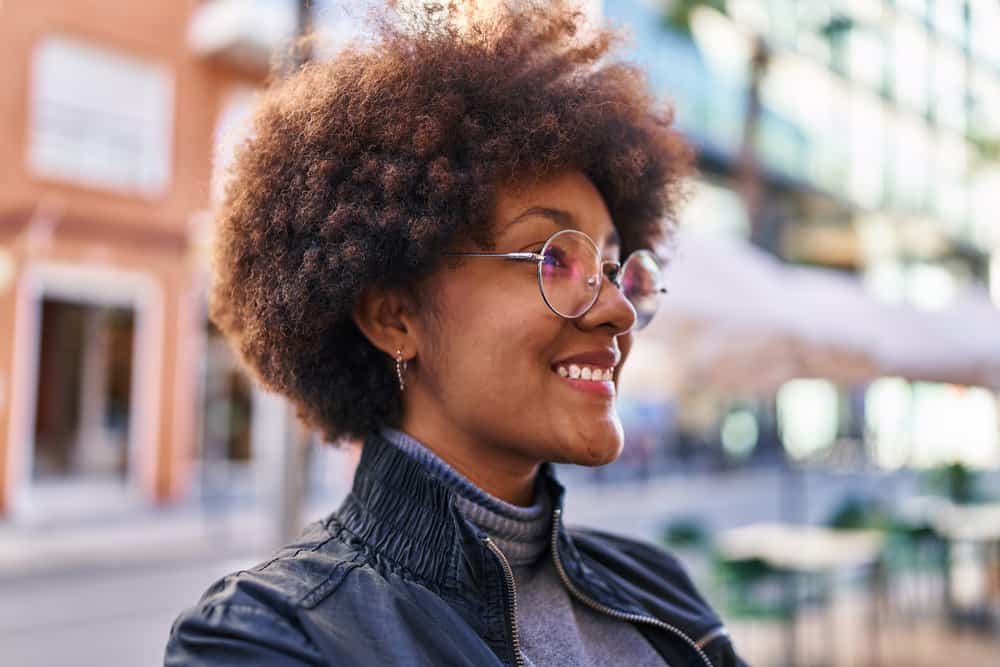 A confident black female with thin curly hair styled with the Curly Girl Method using Ouidad Climate Control Gel.