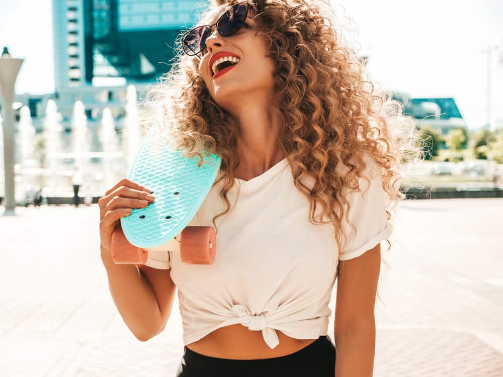 A young white lady with natural curls has a balayage style after finding the right product to create warm tones.