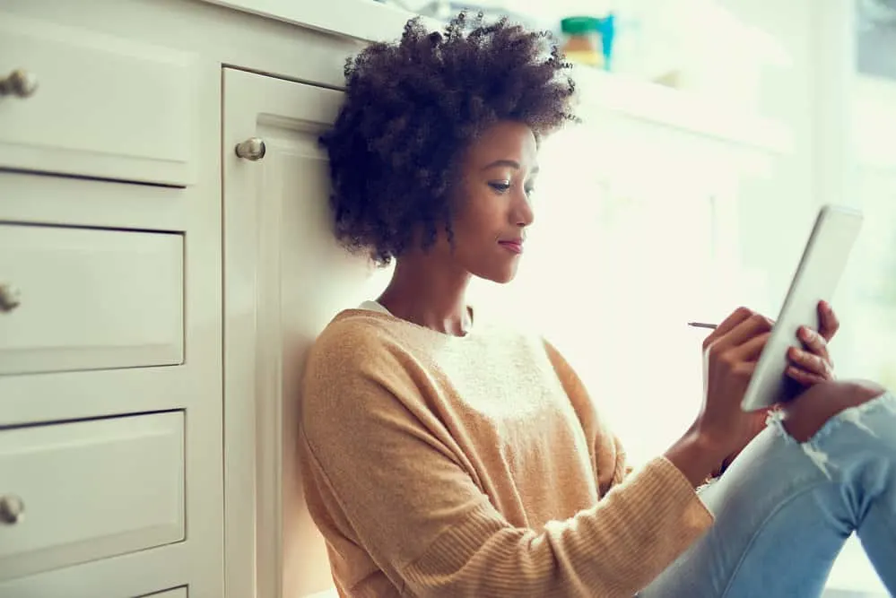 How to Get Rid of Frizzy Curly Hair in 5 Minutes at Home 9 A young female sitting on the kitchen floor using an iPad to read an article about hair frizz.