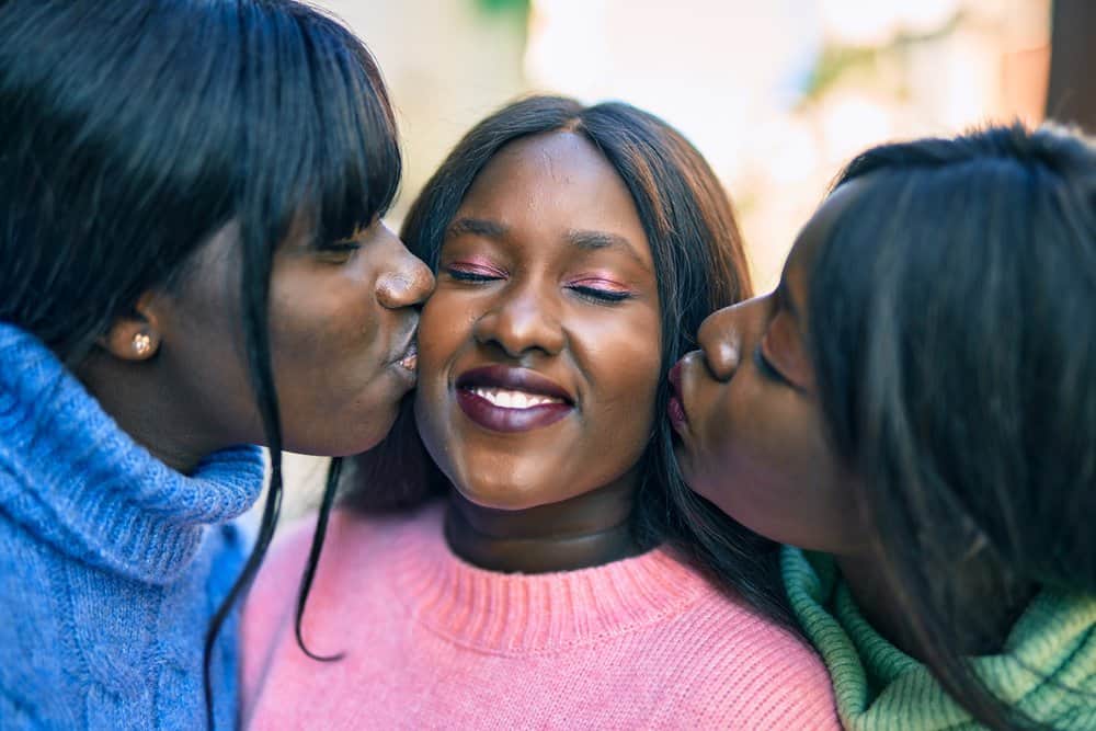 A family of three sisters wearing synthetic lace wigs embraces for a fun family photo. 