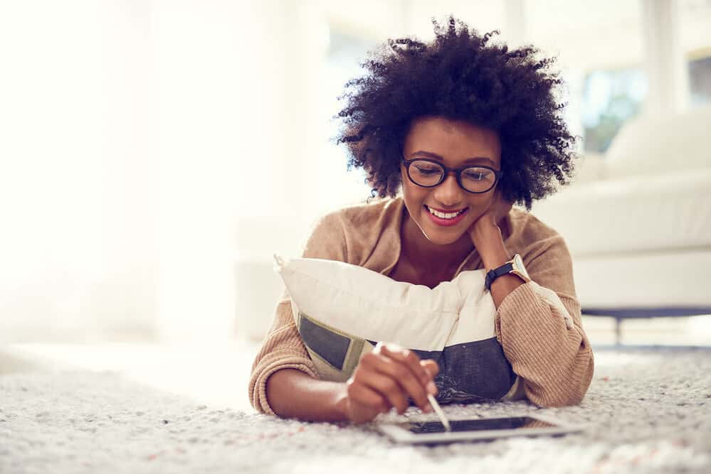 An African female using an iPad at home to purchase a curl cream and olive oil for her hair regimen.