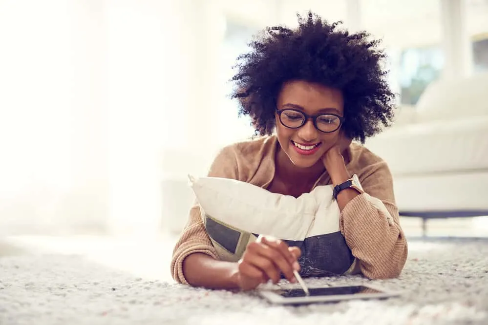 How to Get Rid of Frizzy Curly Hair in 5 Minutes at Home 12 An African female using an iPad at home to purchase a curl cream and olive oil for her hair regimen.
