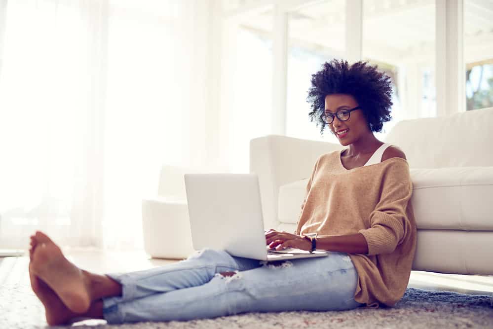 A black female using a laptop to read about creating a hair care routine to fight frizz.