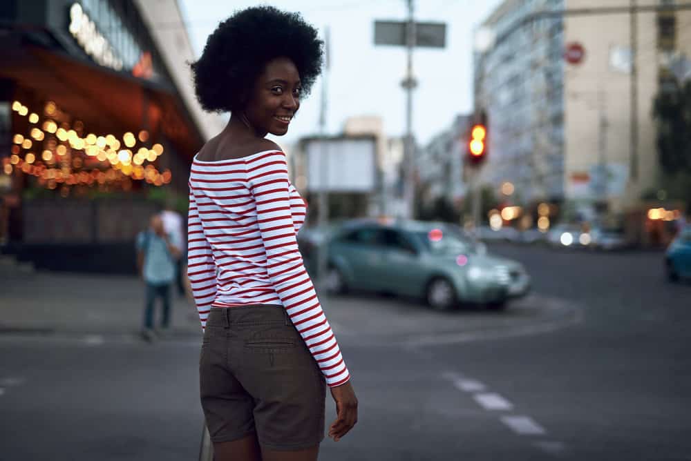 A fashionable African American female wearing a curly afro styled with castor oil to retain moisture.