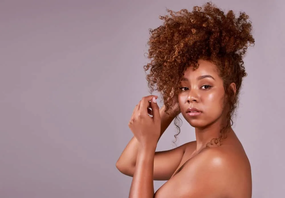 A beautiful black female with naturally curly hair wearing a cute curly hair updo on her unwashed hair with a few hair strands highlighting her beautiful face.