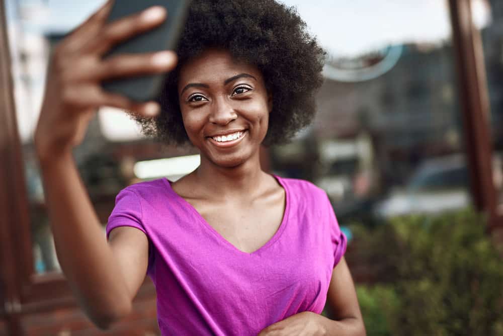 A cute black lady takes a selfie of her more defined curl pattern after using the African Threading Method.