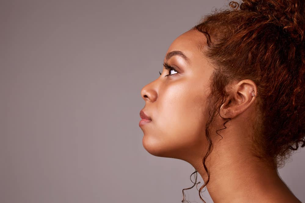 A black female's curly hair is styled in an elegant updo with a few tendrils and loose strands, creating a perfect style for any occasion.