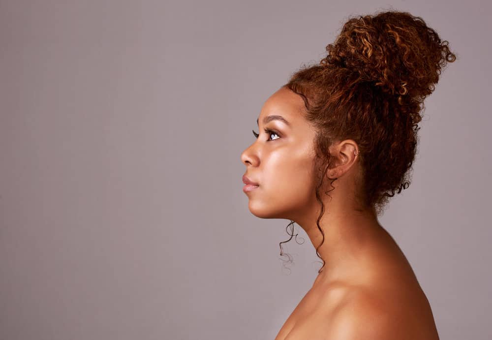 A black female with freshly washed curly hair shows off her hair texture in a cute updo, styled with a few loose curls and hair strands framing her face.