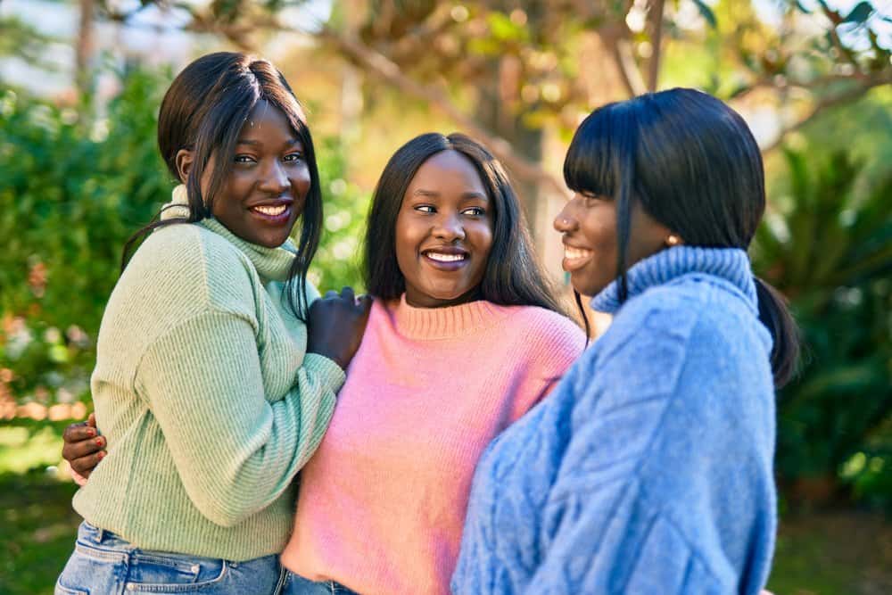 Black girls wearing synthetic lace front wigs have a laugh while they enjoy a summer day.