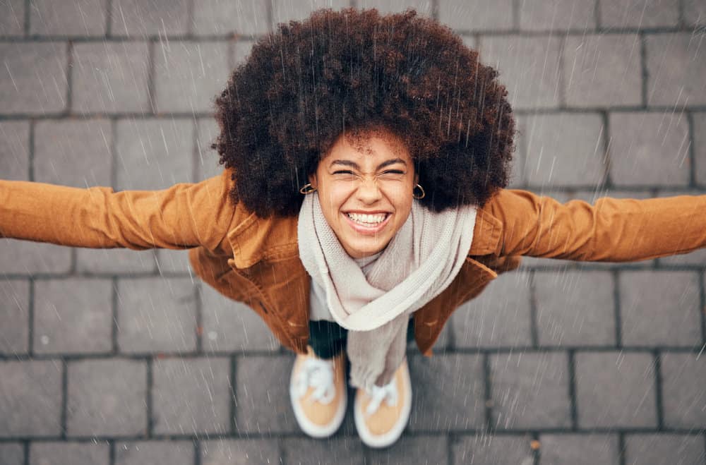 A cute black woman with low porosity hair styled with castor oil standing outside in the rain.