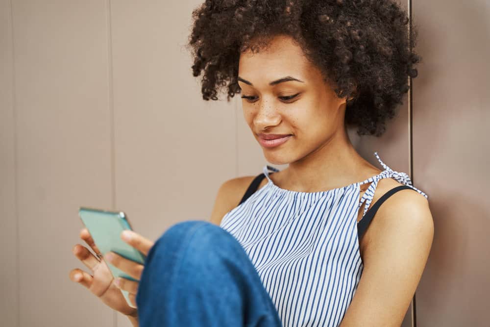 A beautiful African American female using her iPhone to learn about the CG hair care method.