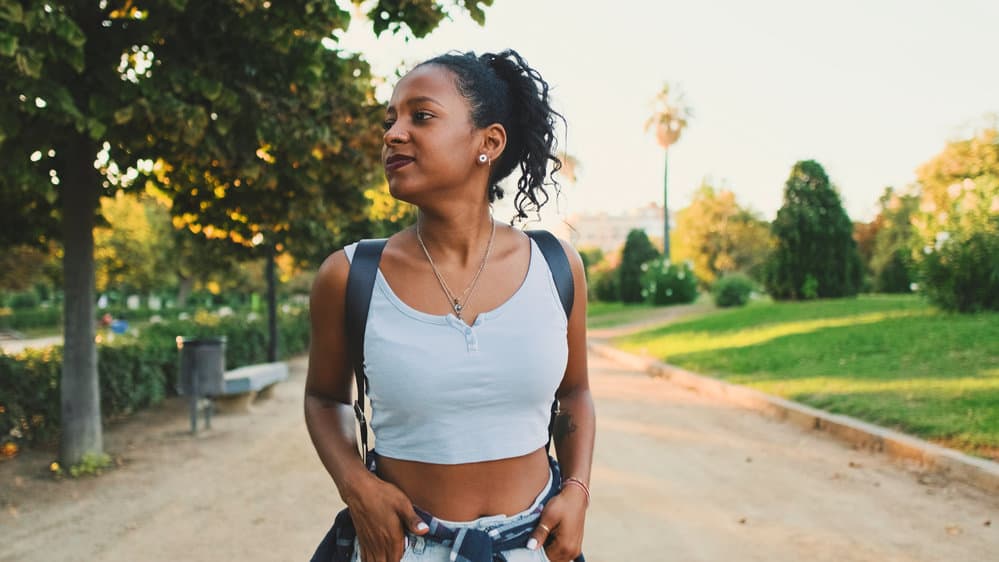 A brown-skin female with beautiful healthy skin wearing her curly hair strands in a ponytail.