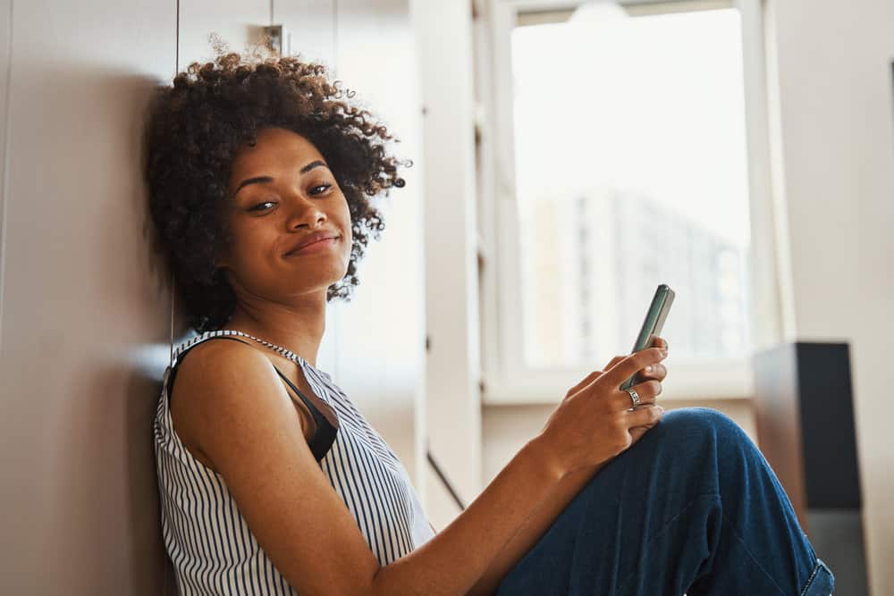 A black female using an iPhone to research how much moisture conditioners provide.