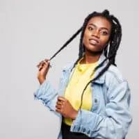 A black lady with freshly washed hair wearing left and right strands uses her right hand to gently pull a braid.