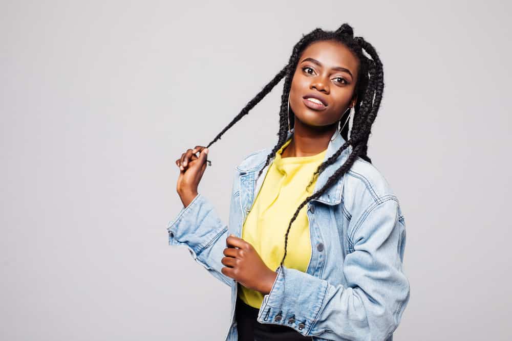 A black lady with freshly washed hair wearing left and right strands uses her right hand to gently pull a braid.