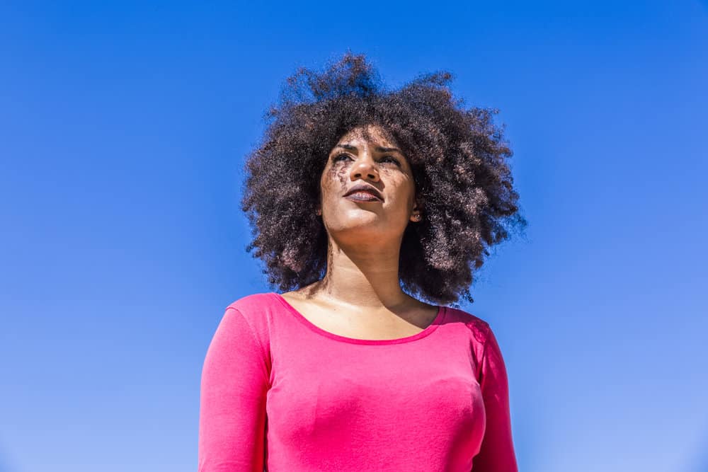 A pretty black woman with dry hair wearing curly bangs created with kitchen scissors.