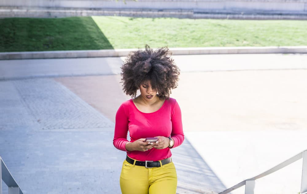 A woman with a curly afro hairstyle is researching how to cut your own hair on her iPhone.