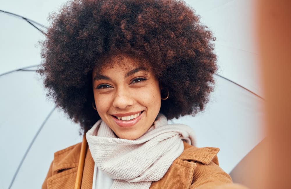 A cute black female wearing a black and brown balayage afro styled with aloe vera juice.