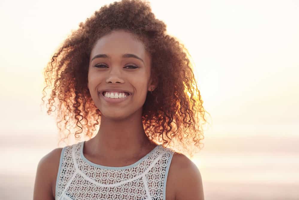 A cute black girl with broken hair strands keeps her hair moisturized with a leave-in deep conditioner.