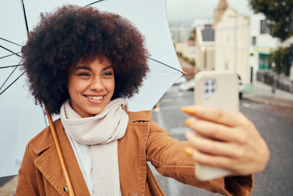 A gorgeous black woman with curly hair strands styled with flax seed gel is taking a selfie.