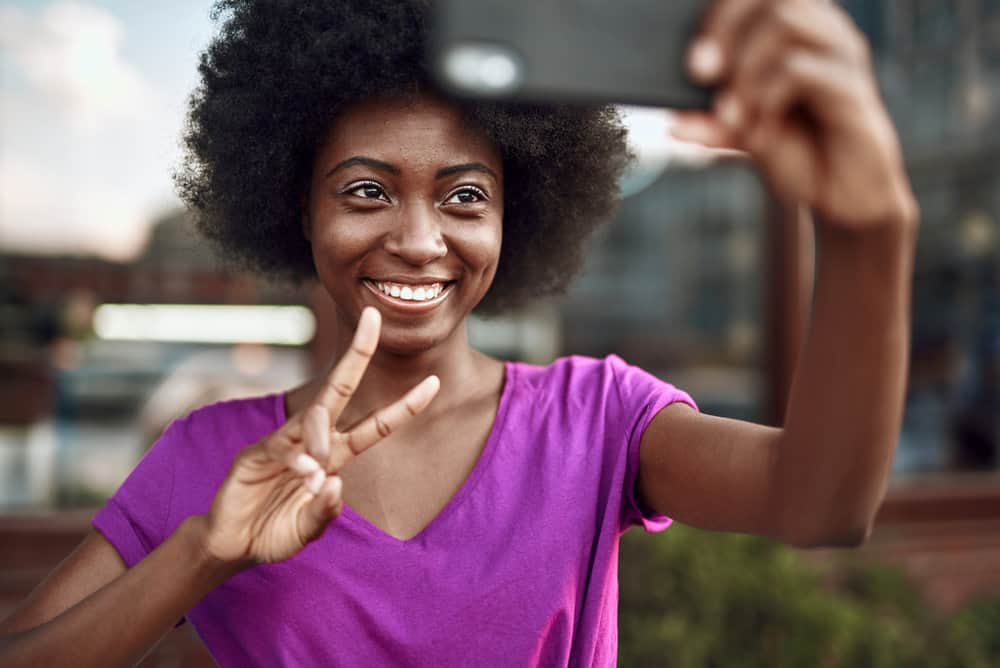 A black woman takes a selfie after stretching hair and styling her curls with coconut oil and coconut milk.